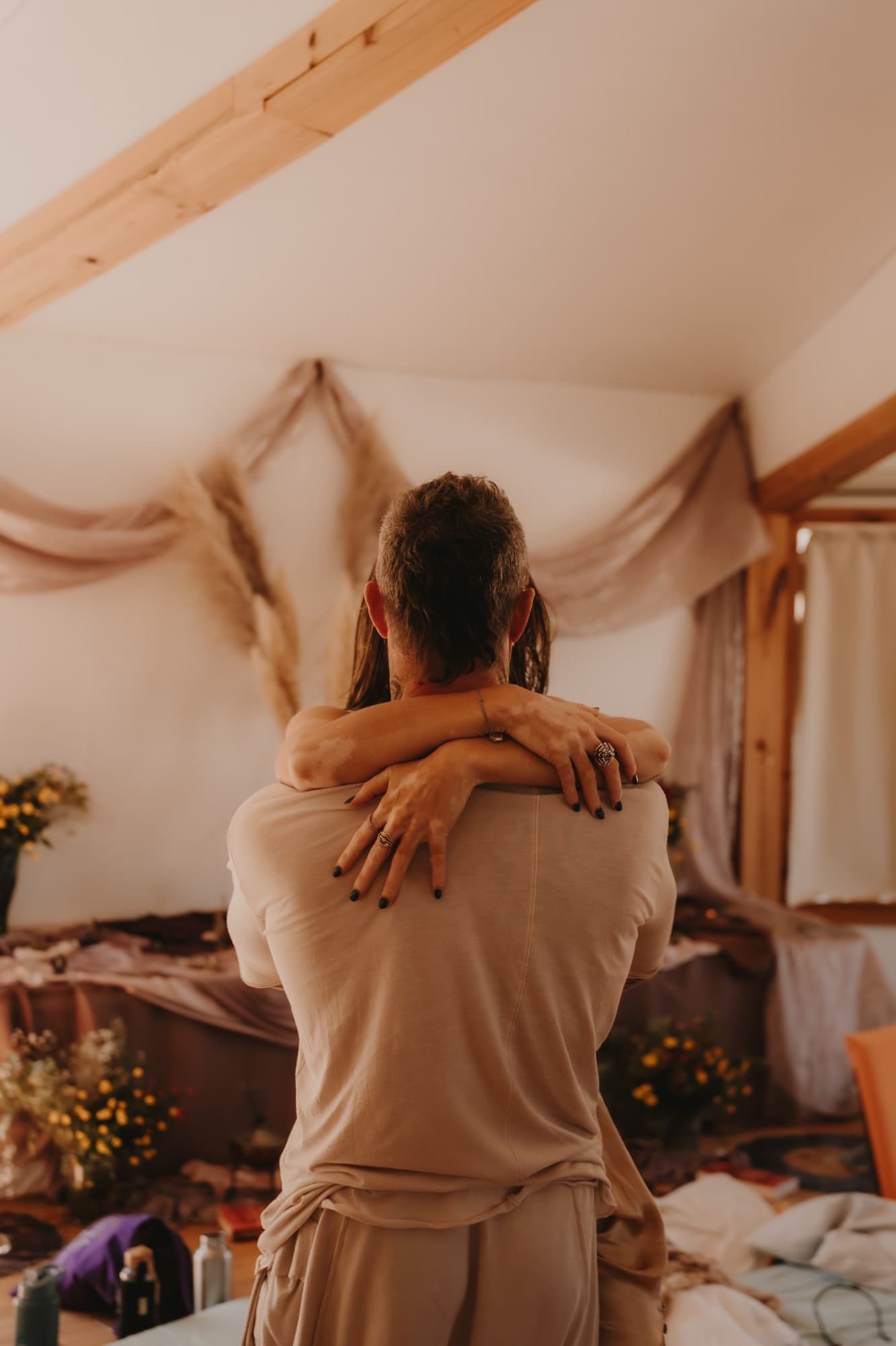 Two people holding each other close, her arms wrapped around his shoulders, in a softly lit room