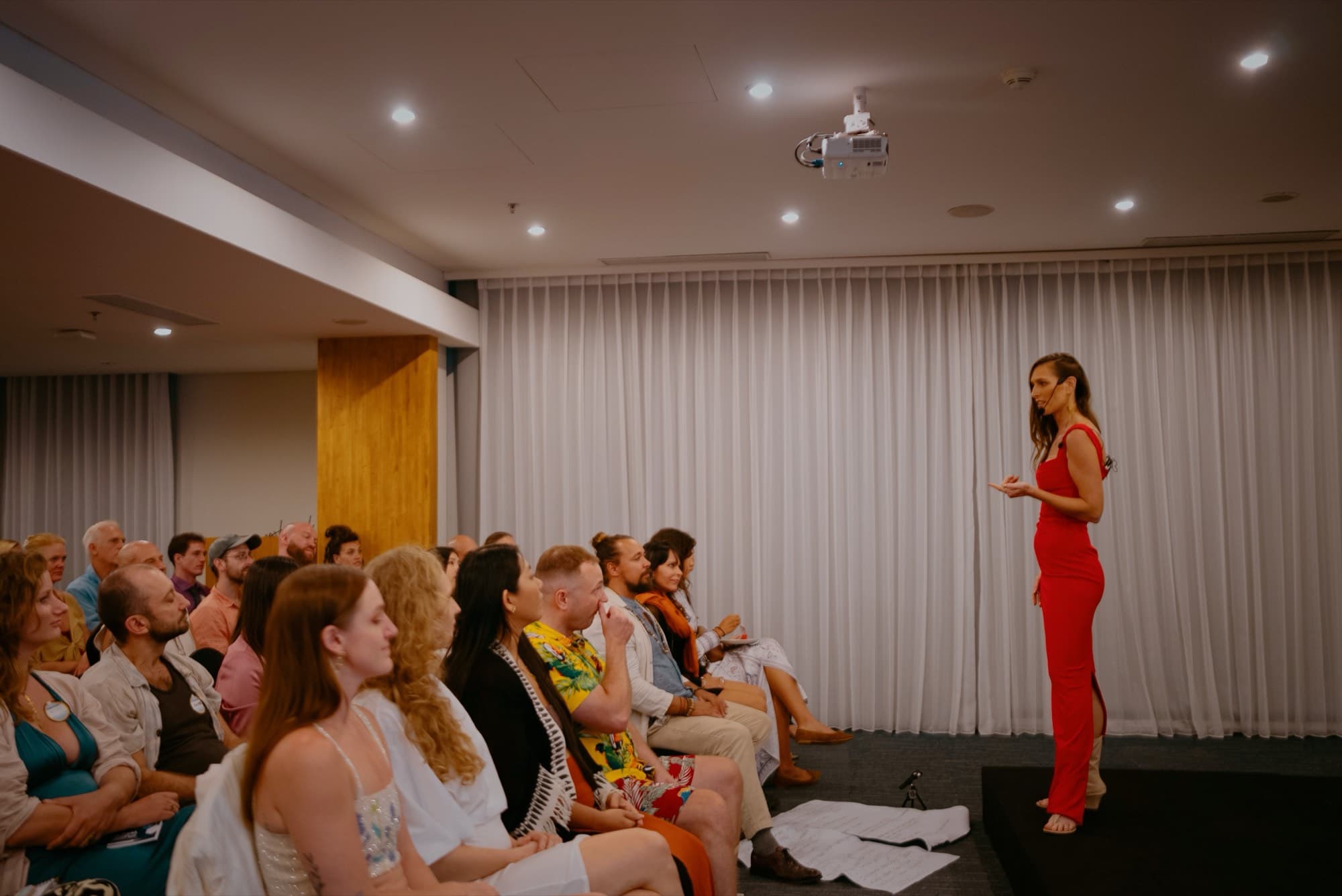 Faces in the audience listening closely, Arja Hendrikx blurred in red in the foreground